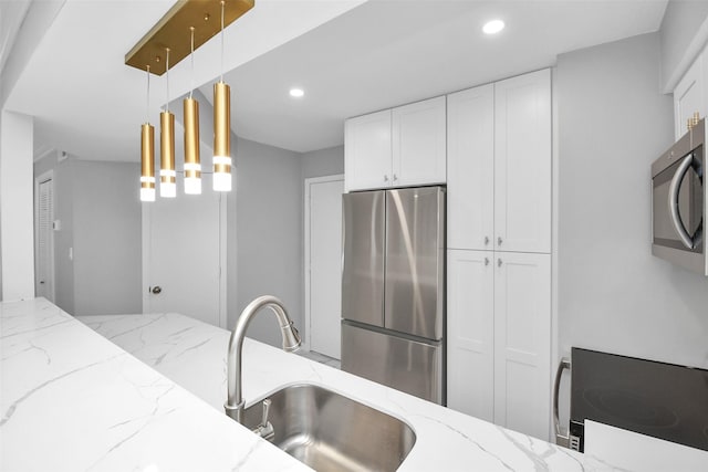 kitchen with sink, light stone countertops, appliances with stainless steel finishes, decorative light fixtures, and white cabinetry