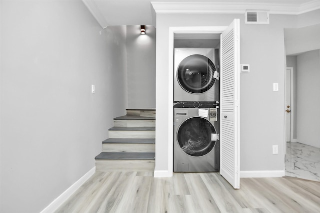 clothes washing area featuring ornamental molding, stacked washing maching and dryer, and light hardwood / wood-style floors