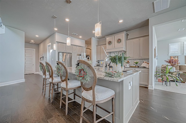 kitchen with light stone countertops, dark wood-type flooring, decorative light fixtures, high end fridge, and a center island with sink