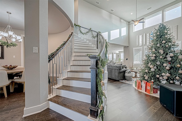 stairway with ceiling fan with notable chandelier, a towering ceiling, and hardwood / wood-style flooring