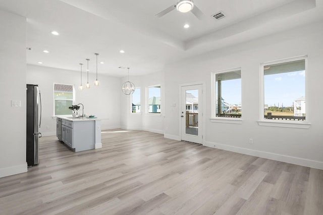 unfurnished living room with light hardwood / wood-style flooring, ceiling fan with notable chandelier, and sink