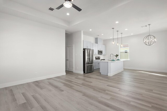 kitchen with light wood-type flooring, stainless steel appliances, a center island with sink, white cabinets, and hanging light fixtures