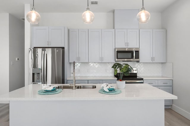 kitchen featuring sink, stainless steel appliances, decorative light fixtures, a kitchen island with sink, and light wood-type flooring