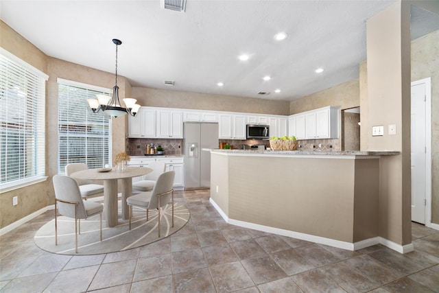 kitchen featuring hanging light fixtures, backsplash, kitchen peninsula, white cabinets, and appliances with stainless steel finishes