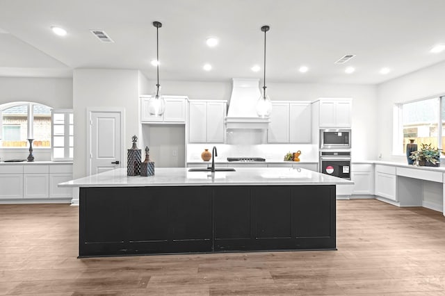 kitchen with built in microwave, an island with sink, premium range hood, and oven