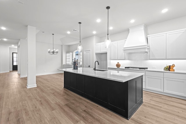 kitchen with sink, white cabinets, a kitchen island with sink, and custom exhaust hood