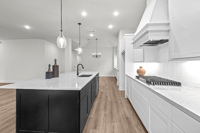 kitchen with premium range hood, a spacious island, decorative light fixtures, light stone countertops, and white cabinets