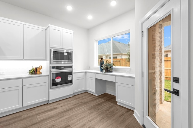 kitchen with light hardwood / wood-style floors, white cabinetry, stainless steel appliances, and built in desk