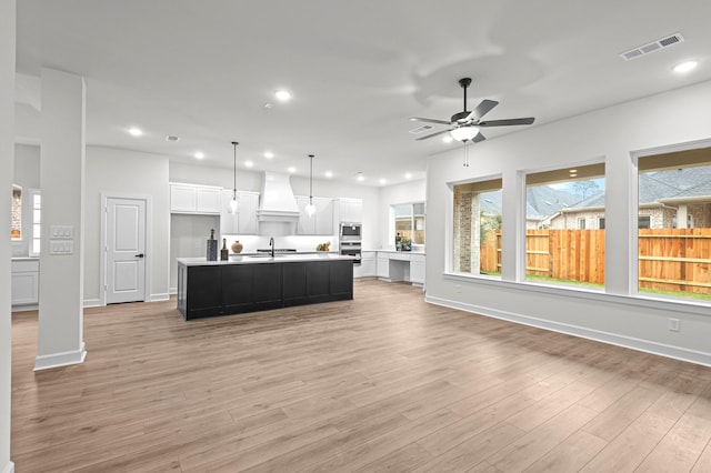 kitchen with white cabinetry, stainless steel appliances, light hardwood / wood-style floors, premium range hood, and a center island with sink