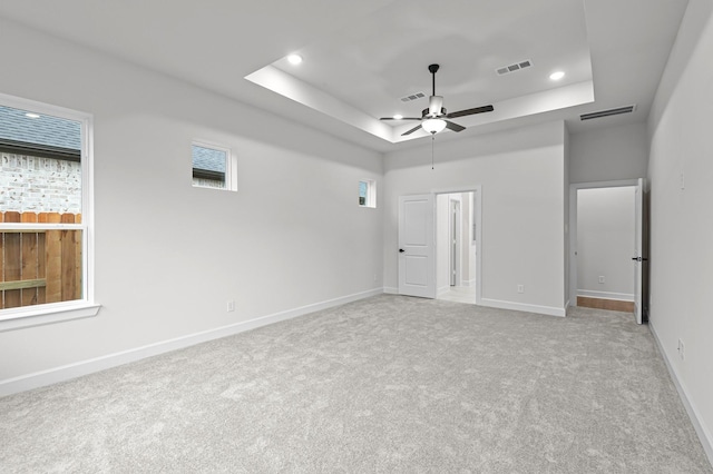 unfurnished bedroom featuring ceiling fan, light carpet, and a raised ceiling