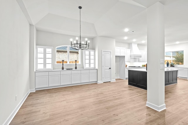 kitchen with custom exhaust hood, white cabinetry, light hardwood / wood-style floors, hanging light fixtures, and a chandelier