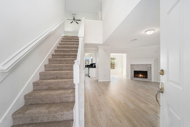 stairs featuring a stone fireplace, ceiling fan, ornamental molding, and hardwood / wood-style flooring