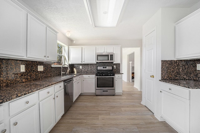 kitchen featuring light wood-type flooring, a textured ceiling, stainless steel appliances, dark stone countertops, and white cabinetry