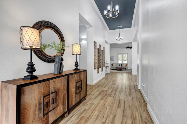 hallway with crown molding, a notable chandelier, and light wood-type flooring