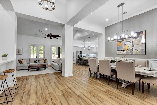 dining room featuring french doors, light wood-type flooring, ceiling fan with notable chandelier, crown molding, and a high ceiling