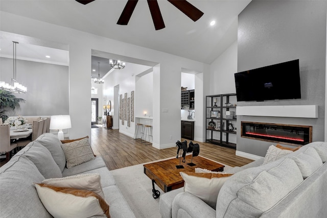 living room with ceiling fan with notable chandelier, wood-type flooring, ornamental molding, and high vaulted ceiling