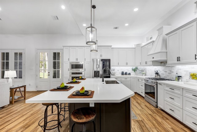 kitchen featuring light wood-type flooring, custom exhaust hood, a breakfast bar, stainless steel appliances, and an island with sink