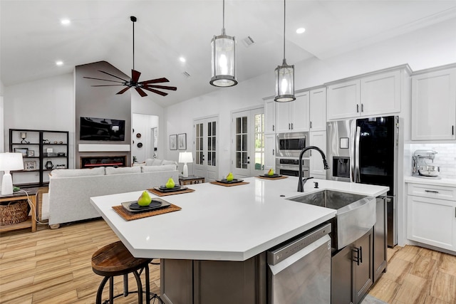 kitchen with a center island with sink, white cabinets, decorative light fixtures, light hardwood / wood-style floors, and stainless steel appliances