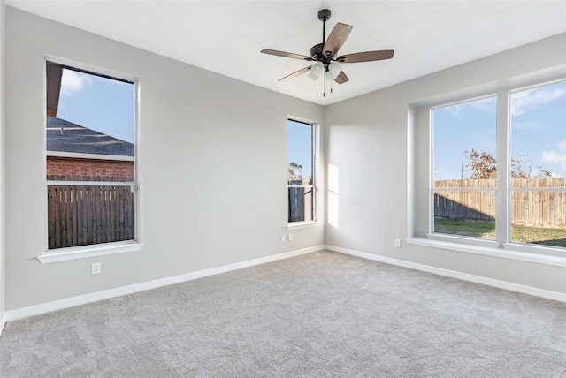 spare room featuring light colored carpet, a wealth of natural light, and ceiling fan