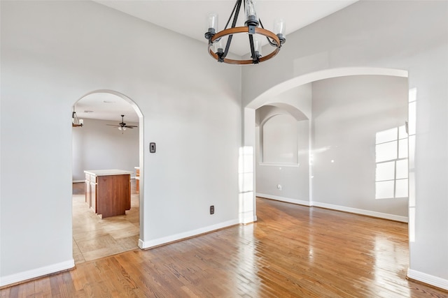 unfurnished room with ceiling fan with notable chandelier, a towering ceiling, and light hardwood / wood-style flooring