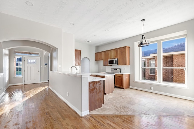 kitchen with range with electric cooktop, sink, hanging light fixtures, a textured ceiling, and light wood-type flooring