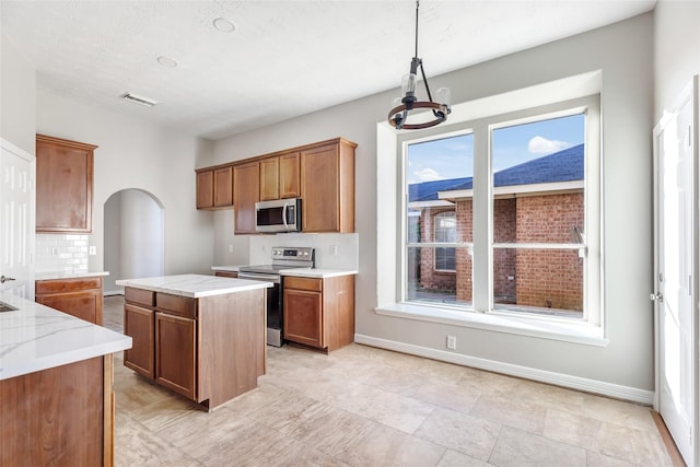 kitchen featuring an inviting chandelier, hanging light fixtures, appliances with stainless steel finishes, tasteful backsplash, and a kitchen island