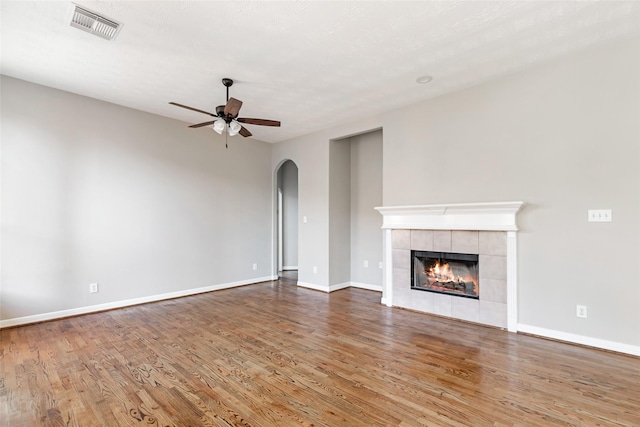 unfurnished living room with a tiled fireplace, ceiling fan, hardwood / wood-style floors, and a textured ceiling