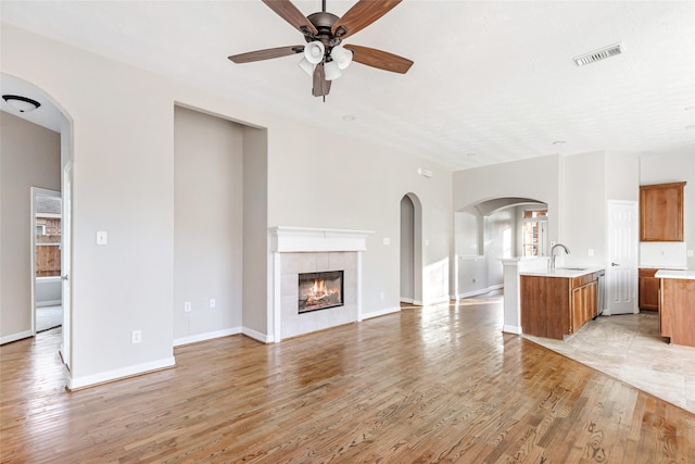 unfurnished living room with ceiling fan, a fireplace, light hardwood / wood-style floors, and sink