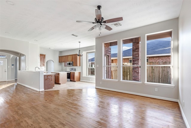 unfurnished living room with a textured ceiling, ceiling fan with notable chandelier, light hardwood / wood-style floors, and sink