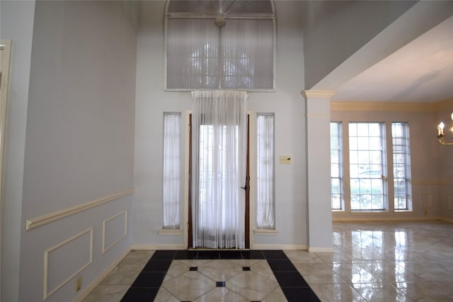 entryway featuring a high ceiling, crown molding, decorative columns, and a chandelier