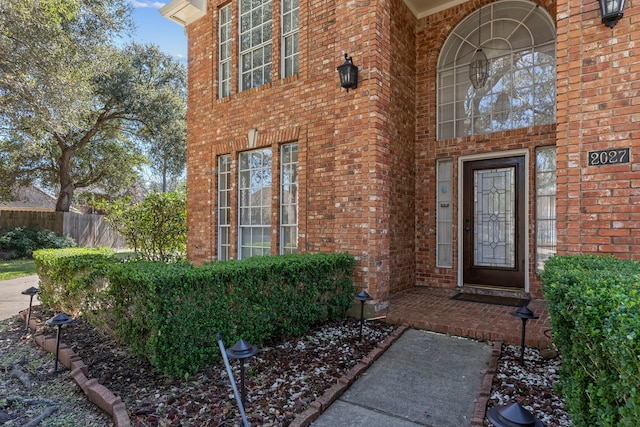 view of exterior entry with brick siding and fence