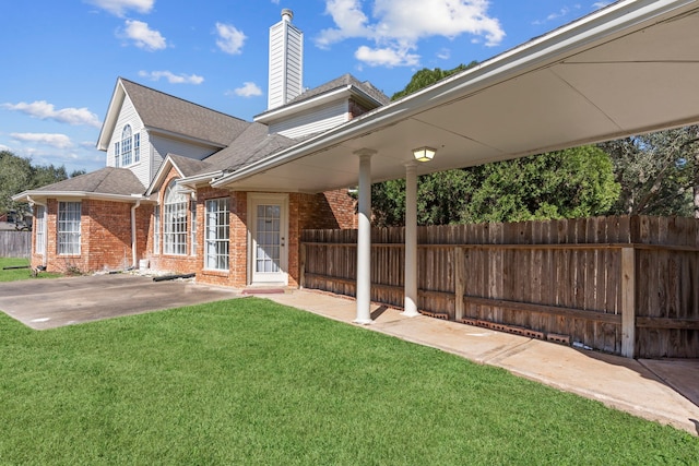 exterior space featuring brick siding, a patio, a chimney, fence, and a front lawn