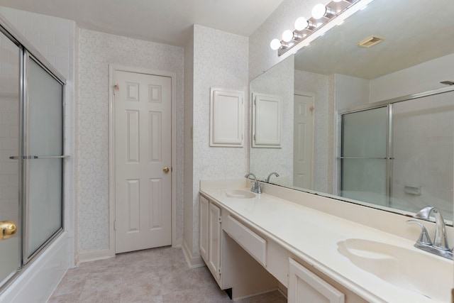 full bath with double vanity, wallpapered walls, shower / bath combination with glass door, and a sink