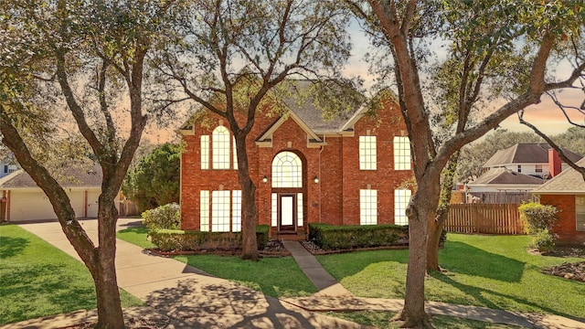 colonial home featuring brick siding, a lawn, and fence