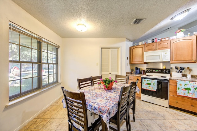 kitchen with a textured ceiling, plenty of natural light, light tile patterned floors, and white appliances