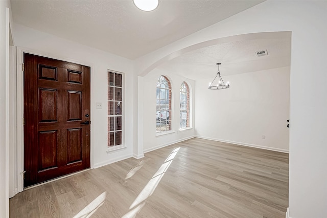 entrance foyer with light hardwood / wood-style floors, a textured ceiling, and a chandelier