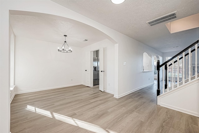 spare room featuring a chandelier, a textured ceiling, and light hardwood / wood-style flooring