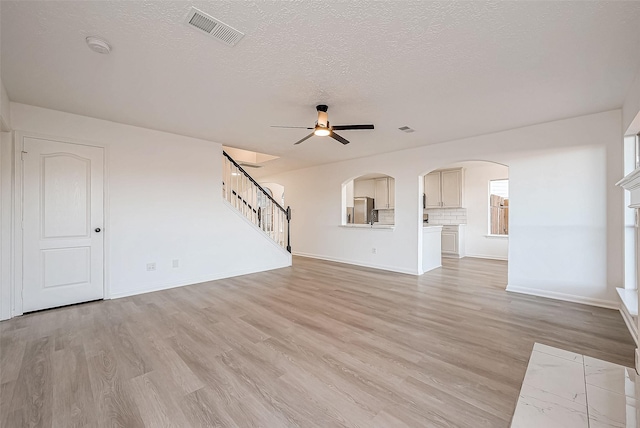 unfurnished living room featuring ceiling fan, light hardwood / wood-style floors, and a textured ceiling