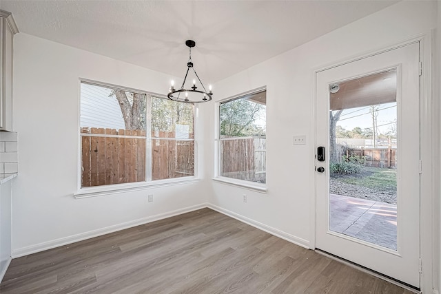 unfurnished dining area featuring an inviting chandelier, a textured ceiling, and hardwood / wood-style flooring