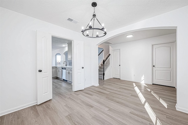 unfurnished dining area with a notable chandelier, sink, a textured ceiling, and light hardwood / wood-style flooring