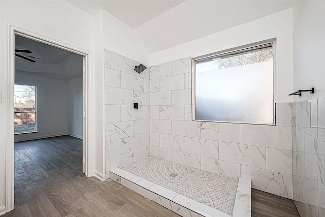 bathroom with vaulted ceiling, ceiling fan, tiled shower, tile walls, and hardwood / wood-style floors