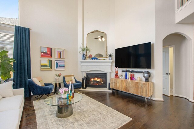 living room with ceiling fan, dark wood-type flooring, and a high ceiling