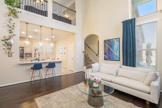 living room with baseboards, arched walkways, hardwood / wood-style flooring, stairway, and a high ceiling