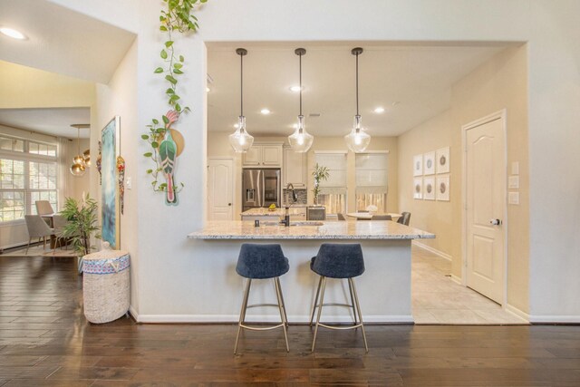 kitchen with pendant lighting, a kitchen breakfast bar, light stone countertops, dark hardwood / wood-style flooring, and stainless steel fridge with ice dispenser