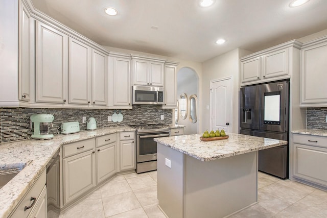 kitchen featuring light tile patterned floors, tasteful backsplash, a kitchen island, light stone counters, and stainless steel appliances