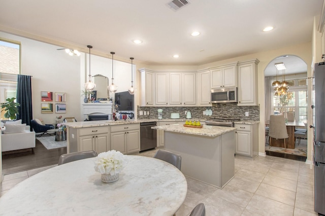 kitchen with light stone countertops, a center island, stainless steel appliances, kitchen peninsula, and pendant lighting