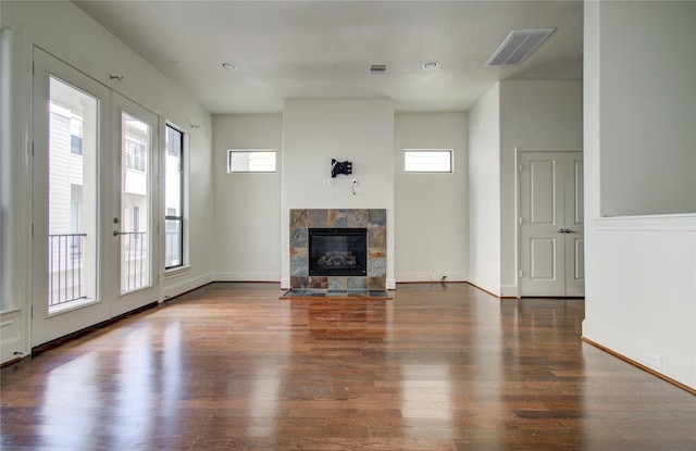 unfurnished living room with a tile fireplace, a wealth of natural light, french doors, and dark wood-type flooring