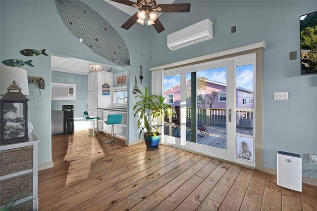 interior space with baseboards, wood-type flooring, ceiling fan, a wall mounted air conditioner, and high vaulted ceiling