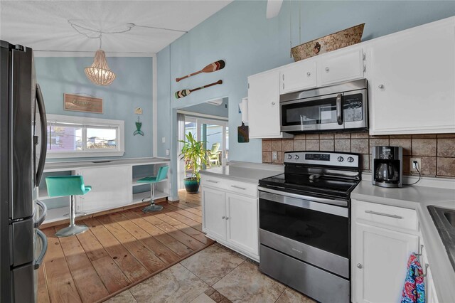 kitchen with a healthy amount of sunlight, white cabinetry, hanging light fixtures, and appliances with stainless steel finishes