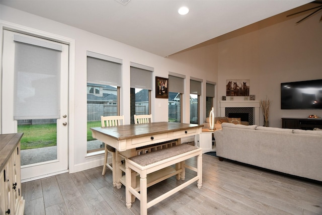 dining area with light hardwood / wood-style floors, lofted ceiling, and a tiled fireplace